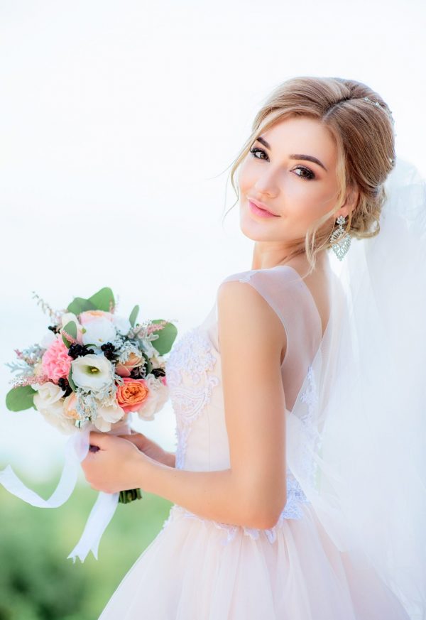 Portrait of a stunning bride with blonde hair holding peach wedding bouquet in her arms