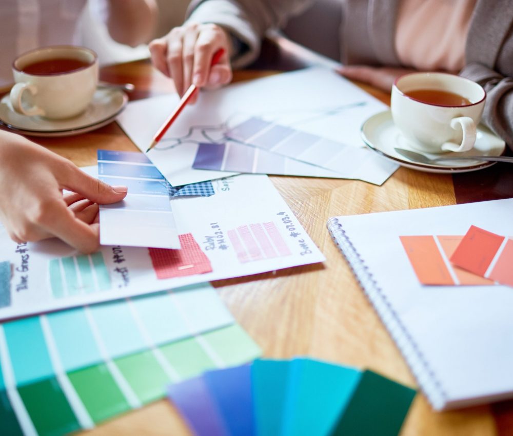 One of fashion designers pointing at swatch of blue tints while explaining her choice to colleague